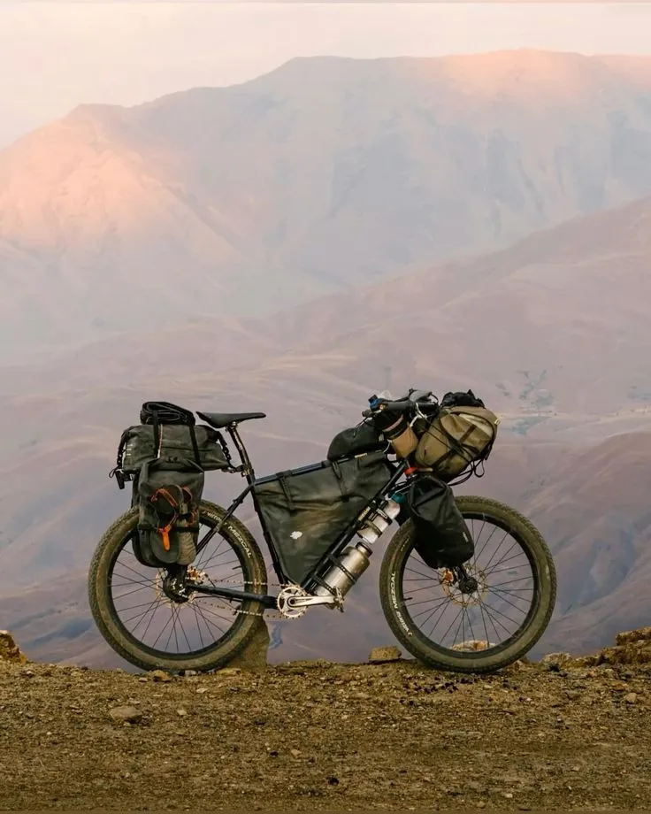 Bicicleta de cicloviaje cargada con alforjas frente a unas montañas al atardecer